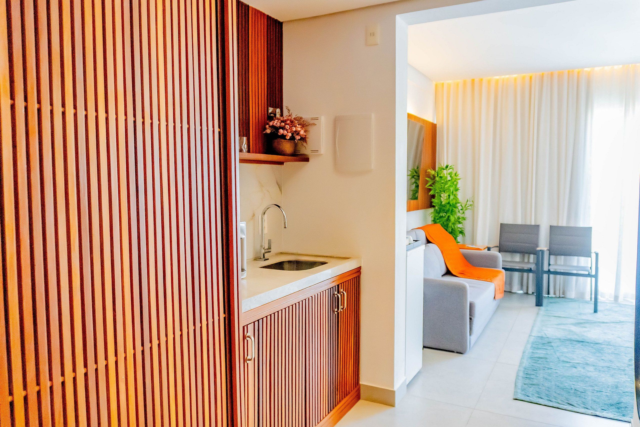 Una cocina moderna con lavamanos y armarios, un comedor con sofá y sillones, y una sala de estar con sofá y una planta.