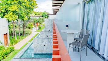 A balcony with a pool, a table with chairs, and a view of the surrounding greenery and buildings.