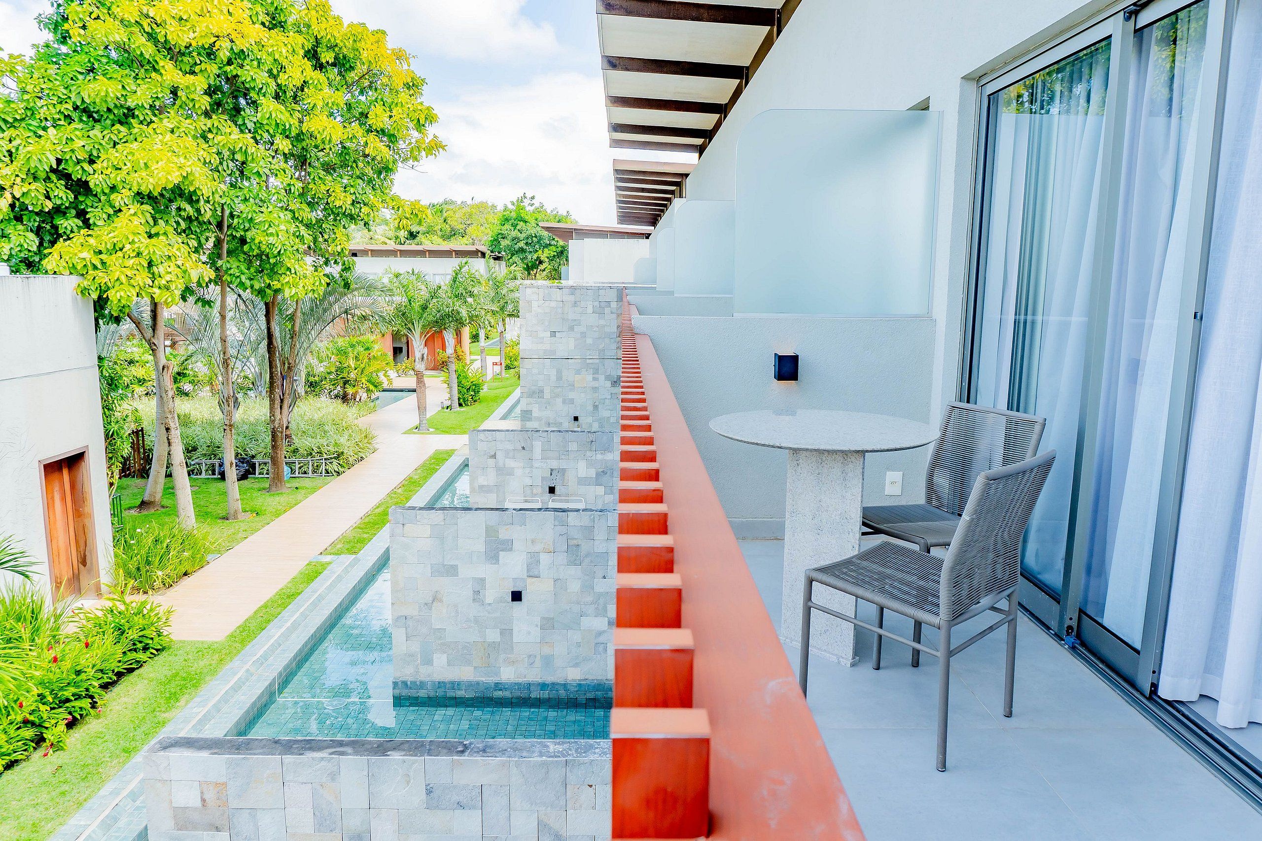 Un balcón con piscina, una mesa con sillas y vistas de la vegetación y edificios circundantes.