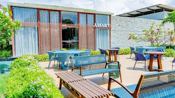An outdoor seating area with tables and chairs, a pool, and a building with a stone wall and a sign that reads 'AMARY GASTRO CLUB'.