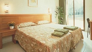 Une chambre d’hôtel avec un grand lit, une table de chevet agrémentée d’une plante, une chaise et une vue sur les arbres par la fenêtre.