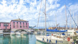 A marina with multiple boats docked, a pink building, and a clear sky. - La casa del Cartografo (Genova)