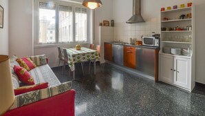A compact kitchen with a dining area, featuring a table with a green and white tablecloth, a red sofa, and a window with blinds. - La casa del Cartografo (Genova)