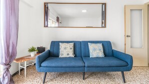 A room with a blue sofa, a small table with a plant, a mirror on the wall, and a door.