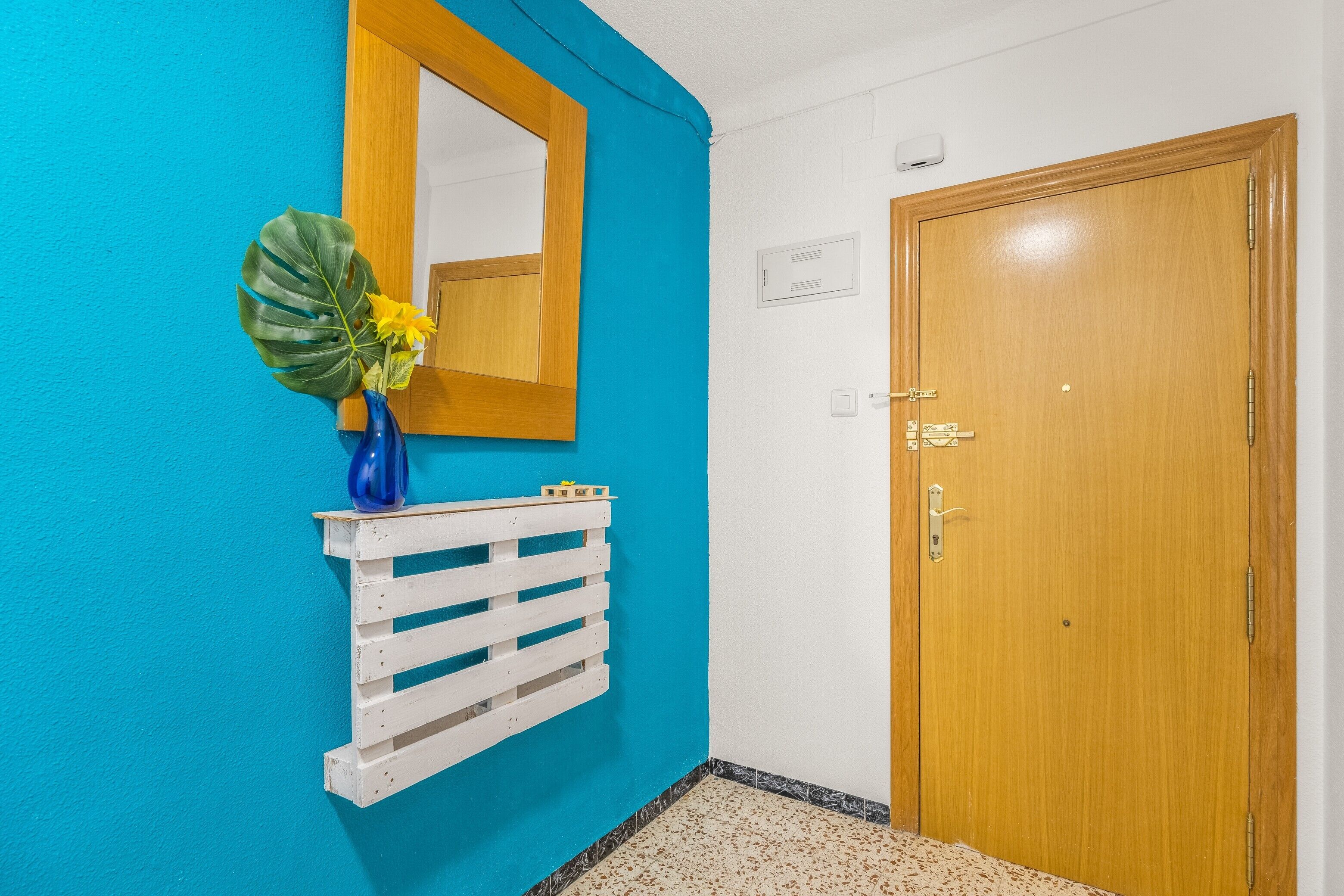 Une pièce avec une porte en bois, un miroir à cadre blanc et un mur bleu.