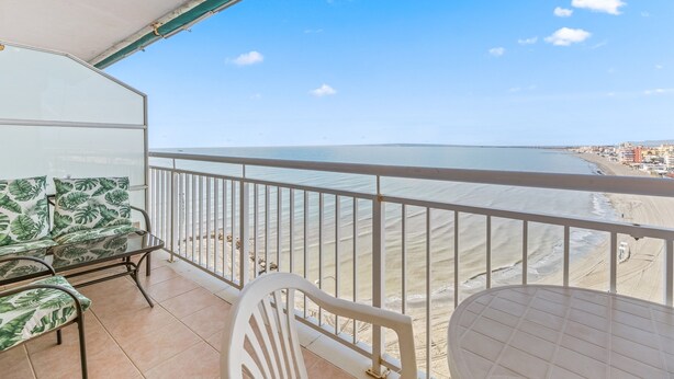 A balcony with a view of the beach and ocean, a table, and a chair.