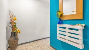 A hallway with a white wall, a blue accent wall, a wooden-framed mirror, a white wooden shelf, and a wicker vase with flowers.