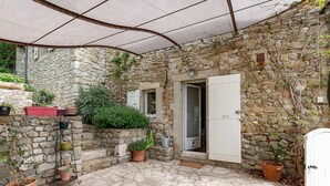 A stone building with a tiled patio, potted plants, and a white door.