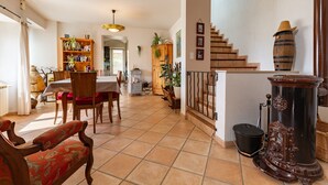 A spacious living area with a dining table, chairs, a staircase, and a decorative stove.