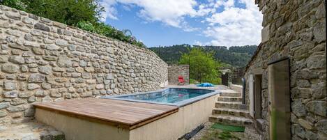 Ein Pool mit Steinwänden und einer Holzterrasse, ein roter Stuhl und Blick auf einen Berg.