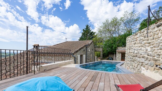 A wooden deck with a swimming pool, stone walls, and a view of the landscape.