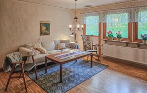 A cozy living room with a sofa, a coffee table, and a chair. There is a window with plants on the sill and a radiator below it. - Awesome home in Brånalt with kitchen (Brånalt)