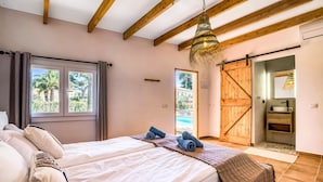 A bedroom with a bed, a wooden ceiling, a large window, and a sliding door leading to a bathroom.