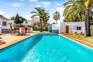 A swimming pool with lounge chairs, palm trees, and a building with a white facade.