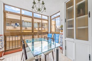 Un espace repas avec une table et des chaises en verre, un lustre et une vue sur les bâtiments voisins.