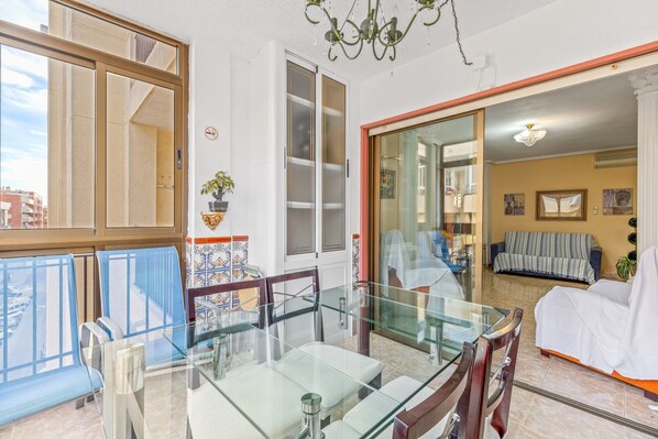 Un espace repas avec une table et des chaises en verre, un lustre et une vue sur la ville grâce à une grande fenêtre.