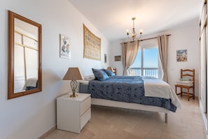 Un dormitorio con cama, mesita de noche, lámpara y una ventana con cortinas.