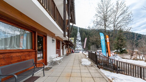 Un bâtiment avec un banc en bois à l’extérieur, un sol recouvert de neige et des drapeaux.