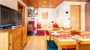 Une pièce chaleureuse avec un plafond en bois, une télévision, un canapé, une table à manger et un coin cuisine.