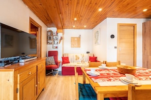 Um quarto acolhedor com teto de madeira, televisão, sofá, mesa de jantar e área de cozinha.