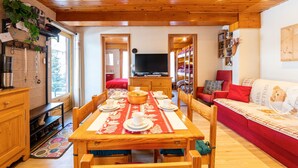 Une pièce aux murs lambrés, avec une table à manger dressée pour quatre personnes, un téléviseur et un canapé rouge.