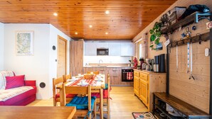 Un intérieur chaleureux avec un plafond en bois, une table à manger avec des chaises, un canapé, un coin cuisine et un porte-chaussures.