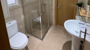 Et moderne badeværelse med brusekabine i glas, toilet og håndvask.
