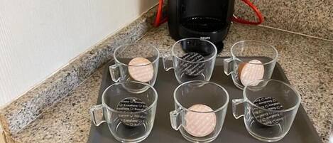 A kitchen counter with a coffee maker, a tray with six glass mugs, and a set of utensils.