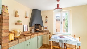 Une cuisine avec une cheminée en briques, une fenêtre donnant sur un beau paysage et une table à manger avec des chaises.