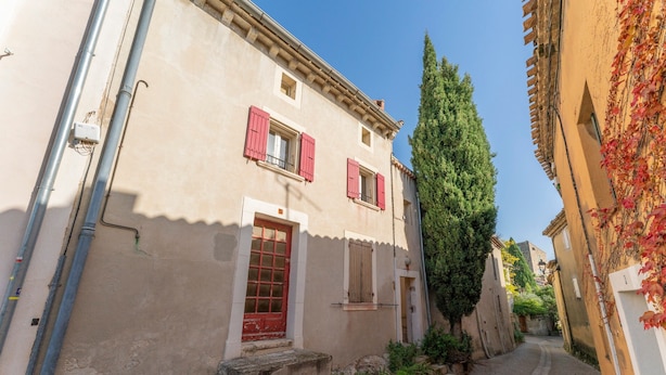 Une rue étroite bordée d’immeubles, avec une porte rouge et un grand arbre.