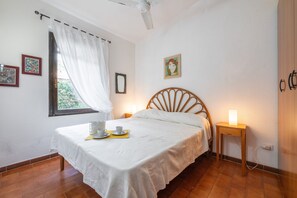 Une chambre à coucher avec un lit, des lampes de chevet, une fenêtre avec des rideaux et des œuvres d’art accrochées aux murs.