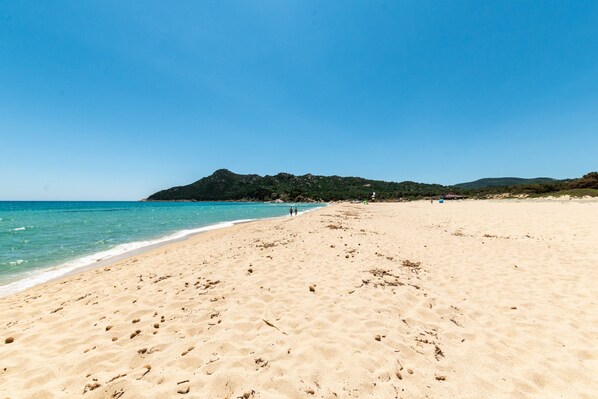 Une plage de sable parsemée d’empreintes, un ciel bleu azur et une colline qui se dessine à l’horizon.
