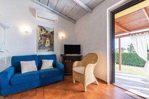 Un salon avec un canapé bleu, un fauteuil en osier, un téléviseur à écran plat et un tableau accroché au mur.