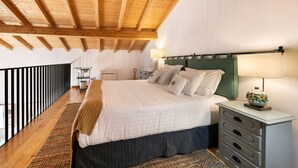 Une chambre avec un plafond en bois, un lit avec une literie blanche, une table de chevet avec une lampe, et une vue sur le balcon extérieur.