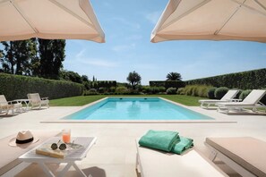 A swimming pool with lounge chairs and umbrellas, surrounded by greenery.