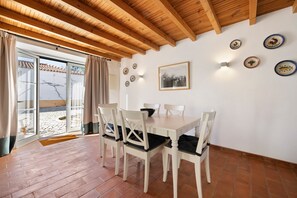 A dining area with a wooden ceiling, white walls, and a tiled floor.