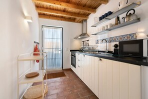 A kitchen with white cabinets, a black microwave, and a window with a curtain.