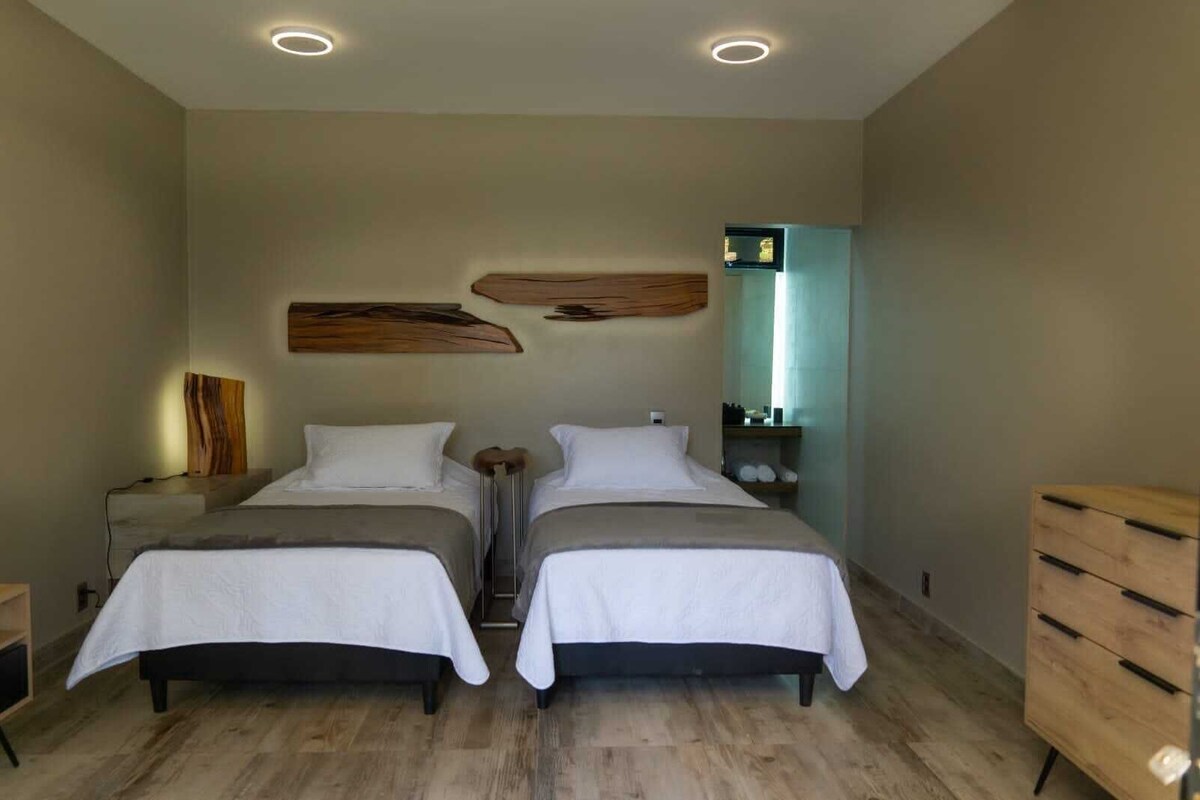 A double room with two beds, a wooden dresser, a nightstand, and a wall-mounted mirror.