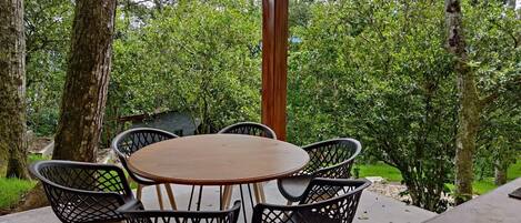Un patio exterior con una mesa redonda y sillas, rodeado de árboles y follaje.