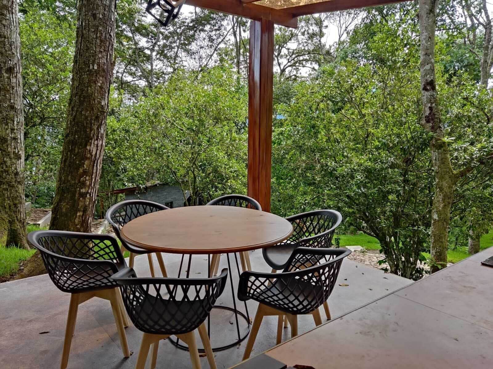 Un patio al aire libre con una mesa redonda y cuatro sillas, rodeado de árboles y follaje.