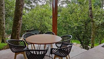 Un patio al aire libre con una mesa redonda y cuatro sillas, rodeado de árboles y follaje.