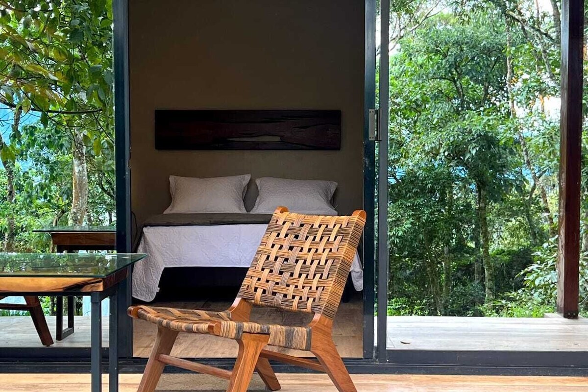 A room with a bed, a wicker chair, and a glass table.
