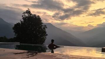 Une personne assise sur un banc au bord d’un lac, avec des montagnes en arrière-plan.