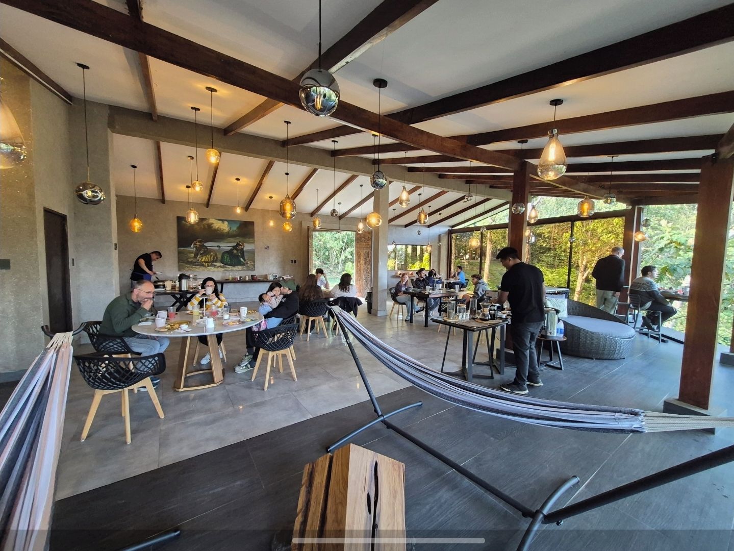 An indoor dining area with wooden beams, hanging pendant lights, and a view of the outdoors.
