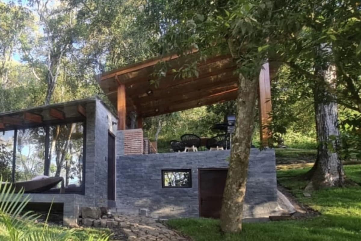 A modern outdoor structure with a wooden pergola, stone walls, and a seating area.
