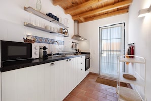 A kitchen with white cabinets, a black countertop, a microwave, a stove, and a hanging rack with kitchen utensils.