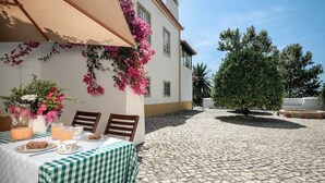 Un patio con una mesa lista para el desayuno, una pérgola adornada con flores y un árbol.