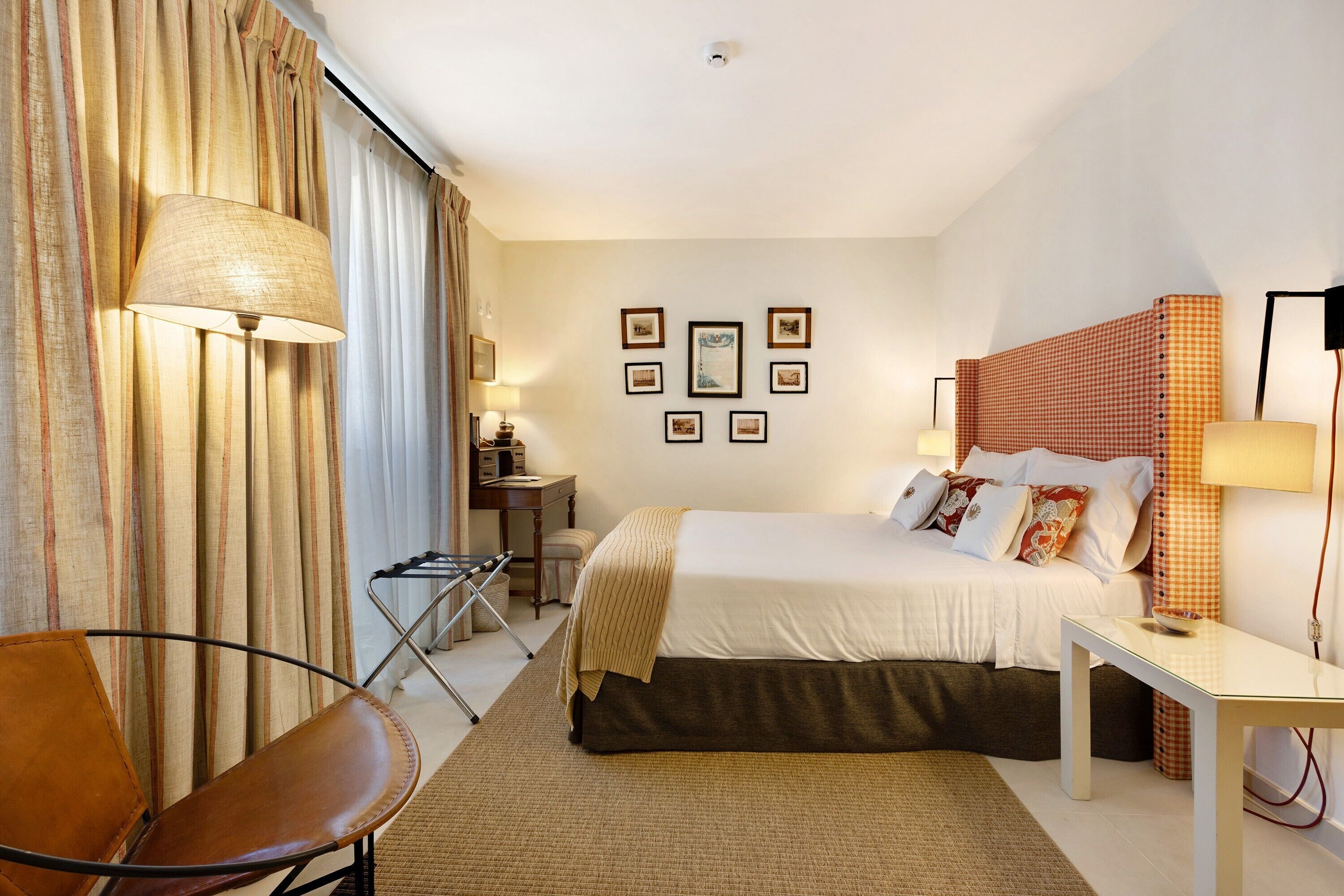 A hotel room with a bed, a desk, a chair, and a lamp.