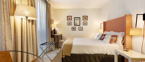 A hotel room with a bed, a desk, a chair, and a lamp.