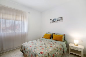 Una camera da letto con un letto, un comodino, una lampada e una finestra con tende leggere.